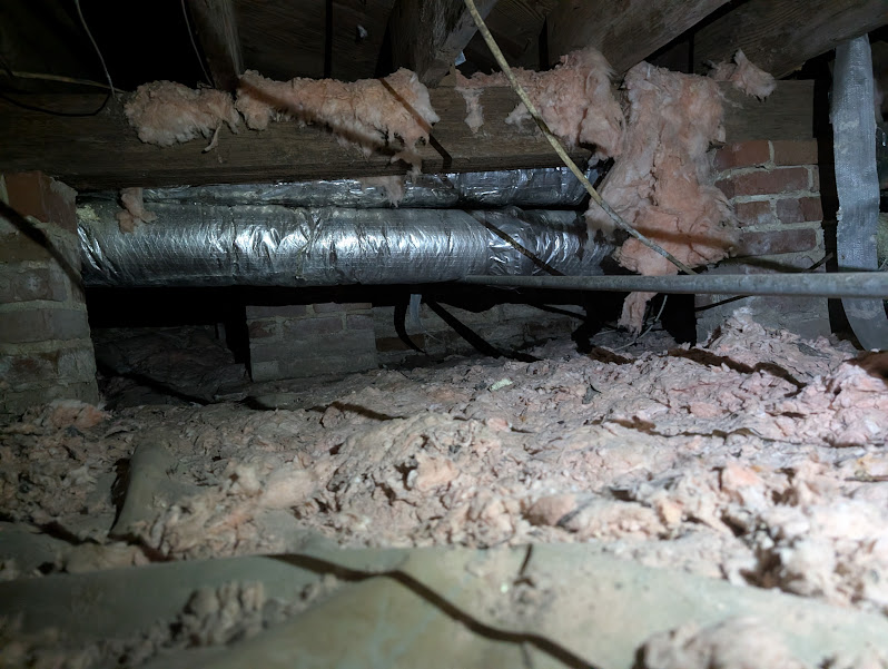 Fallen insulation and old ductwork over bare soil in a brick pier crawlspace