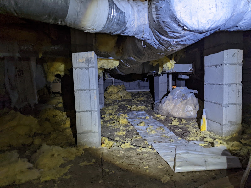 Debris and torn insulation scattered across a crawlspace before cleanout