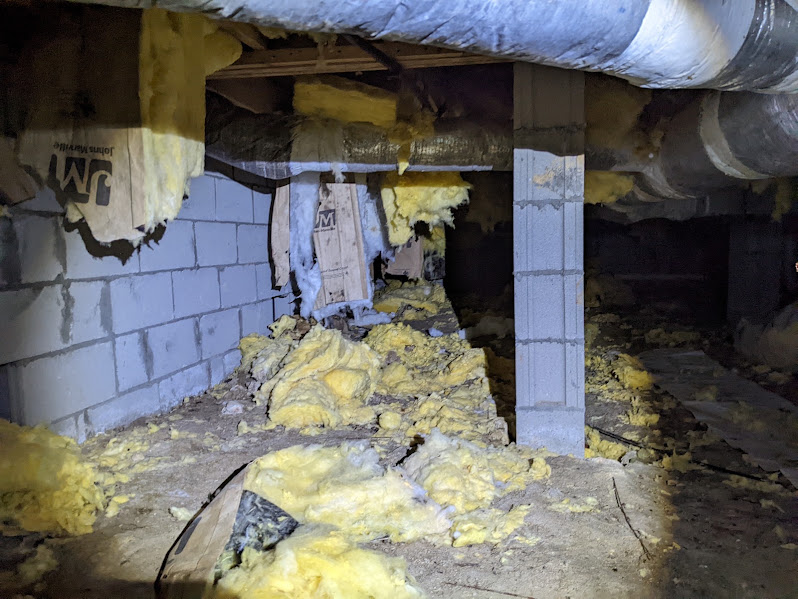 Wet fiberglass insulation fallen from the subfloor onto bare crawlspace soil